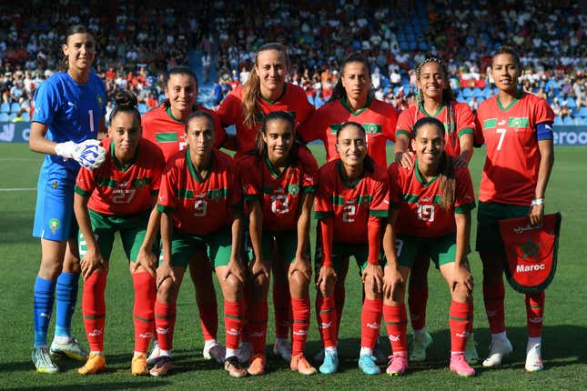 A portrait of the Morocco women's team on the pitch in their red and green jerseys, the goalie on the left in blue.