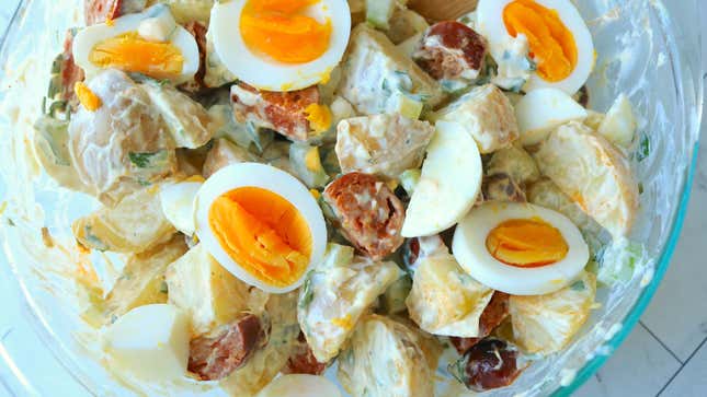 A bowl of potato salad with sliced chorizo and hardboiled eggs.
