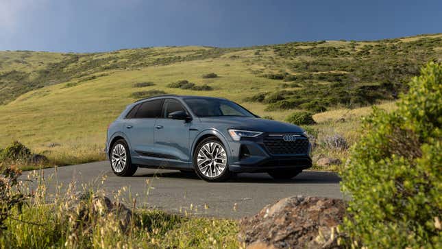 A gray-blue 2024 Audi Q8 E-Tron SUV is parked in front of green, rolling hills.