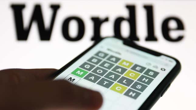 A player attempts Wordle on their phone in front of a white background with "Wordle" written in black text.