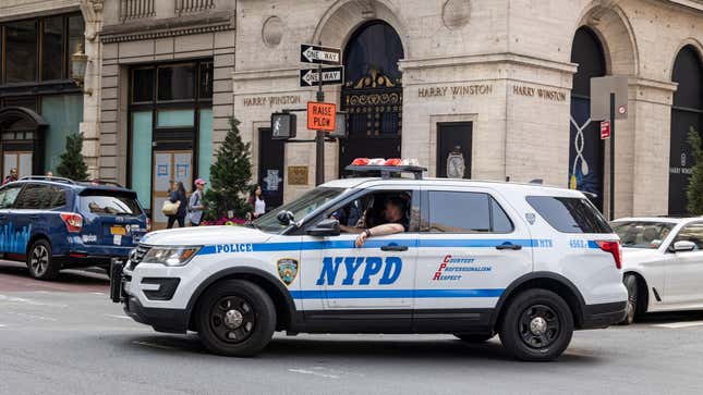 Parked and moving New York City Police Department vehicles on the road are spotted moving in the traffic or parked along the street of the Fifth Ave with the NYPD logo on the side of the car and the inscription Courtesy Professionalism Respect CPR.