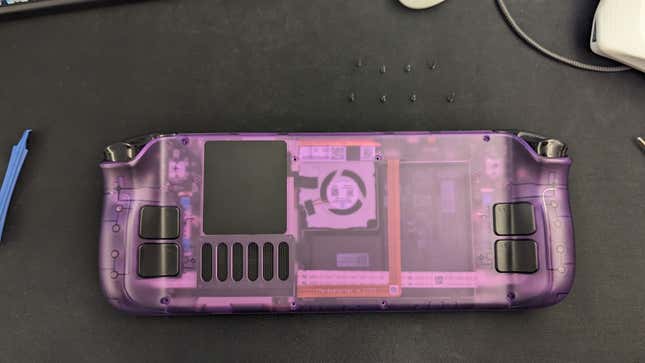 A Steam Deck with a purple back plate sits next to screws and a tool.