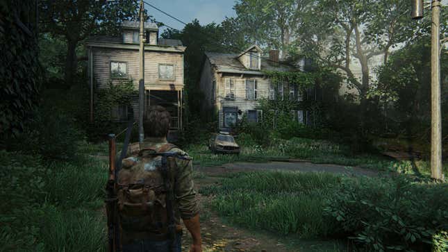 Joel stands facing old, dirty, overgrown houses on a grass-covered street in the game The Last of Us.