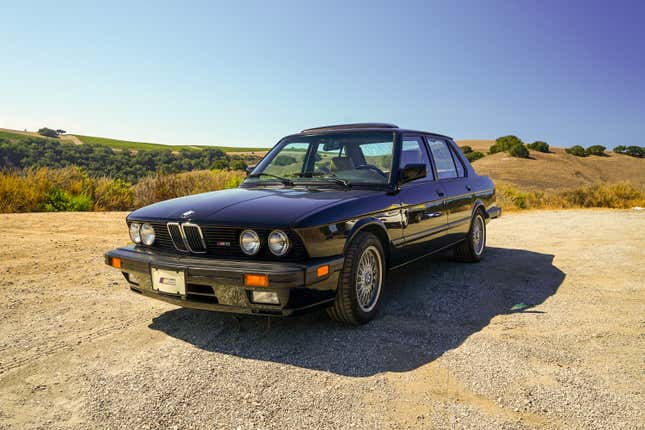 A black BMW M5 parked on gravel.