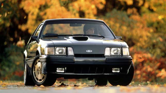 A photo of a black Ford Mustang surrounded by trees. 
