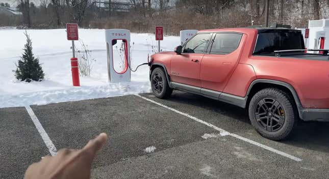 A red Rivian R1T is charging at a Tesla Supercharger location with Marques Brownlee pointing at it.