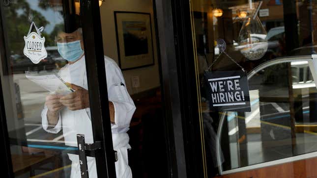 Worker at entrance of restaurant, standing next to "We're hiring!" sign.
