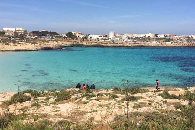 A group of migrants temporarily housed in the shelter, sits by Cala Guitgia, Lampedusa.