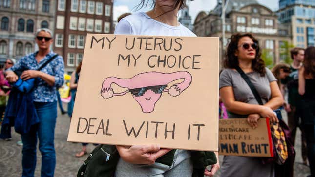 Woman holding pro-choice protest sign reading "my uterus, my choice, deal with it" and showing a uterus with sunglasses in the style of the "Deal with it" meme