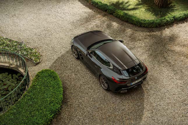 A brown BMW shooting brake concept is parked on gravel near lush forests.  You are looking down at it from above.