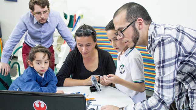 At CIREC, Staffmembers and Dario’s sister and mother and Dario read directions together to figure out how to build a backhoe. At far right, Carlos Arturo Torres Tovar sets up the session.
