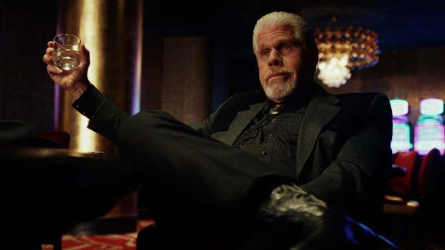 Ron Perlman sits at a poker table and holds a glass of whiskey in Poker Face