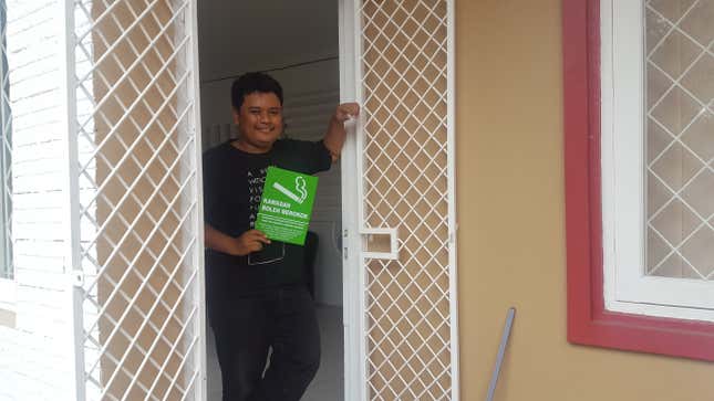 Aditia Purnomo stands outside his office in west Jakarta with a sign saying, “Smoking is a legal activity that is protected by the law.”