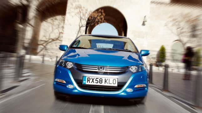 A photo of a blue Honda Insight driving through a city. 