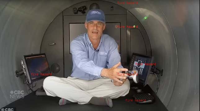 Stockton Rush sits inside a dull metal tube. He has no shoes on and wears black socks, white khaki pants a blue button up and a denim baseball cap