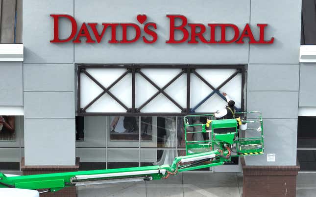 A painter is seen on an industrial lift working on the exterior of a David's Bridal store.