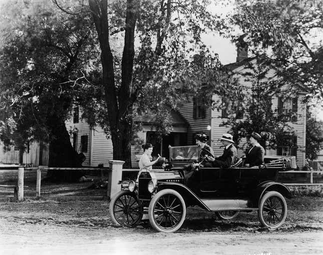 A group of friends in their Model T Ford car collecting something from a woman at a farm, perhaps water to cool the engine. 