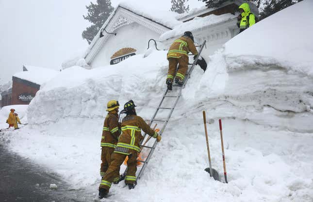 Mammoth Lakes Fire Department firefighters use a ladder on a snowbank while responding to a propane heater leak and small fire at a shuttered restaurant surrounded by snowbanks on March 12, 2023 in Mammoth Lakes, California. 
