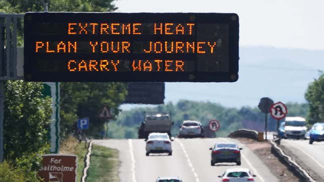 A sign above a highway filled with cars shows a warning message about the extreme heat.