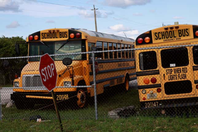 Yellow school buses are shown parked at a depot behind a chain link fence. 