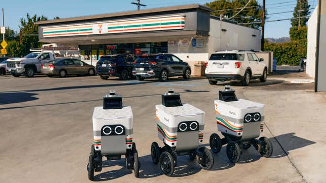 Delivery robots in front of a parking lot at a 7-Eleven.