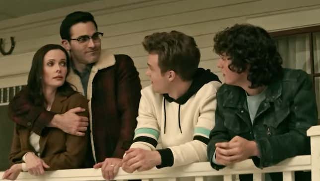 While standing on their porch, Clark Kent hugs Lois Lane as their two teenage sons look on.