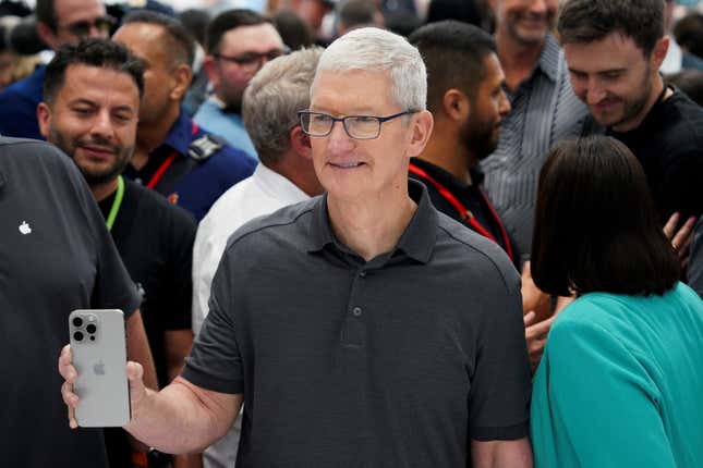 Tim Cook holding an iPhone 15, which is silver with many camera bubbles on the back.