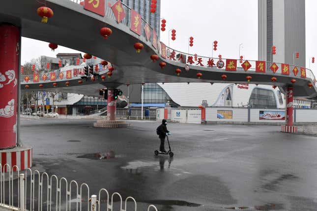 Man wearing a face mask rides a kick scooter through an intersection in Wuhan