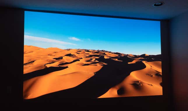 A scene featuring sand dunes and a blue sky projected onto a wall by the JMGO N1 Ultra projector.