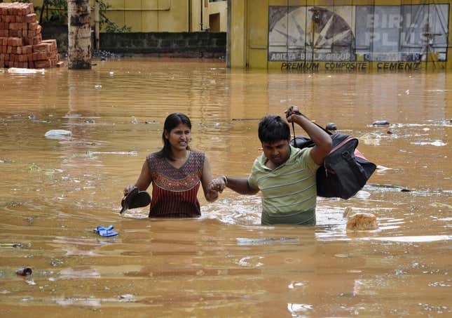 Residents wade through a flooded road as they move to a safer location after heavy rains at Guwahati