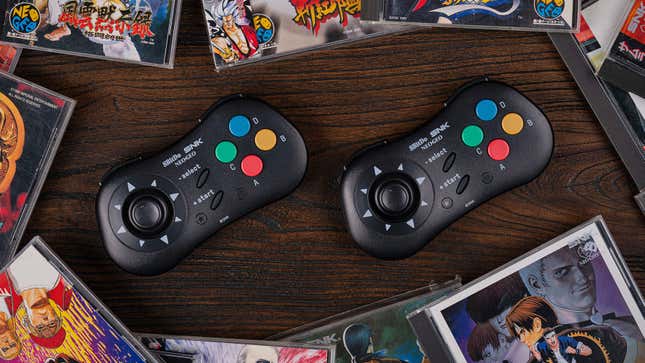 Two 8BitDo NEOGEO CD Wireless Controllers sitting on a wood table surrounded by NEOGEO CD games in jewel cases.