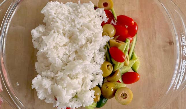 Rice in a bowl with chopped cucumbers, tomatoes, and olives.