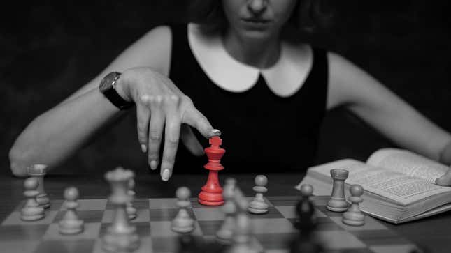 A black and white picture shows a woman touching a red chess piece.