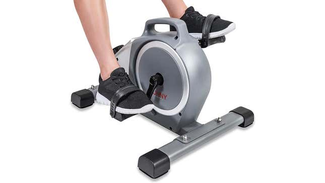 A person's lower legs and feet shown using a compact, pedals-only exercise bike.