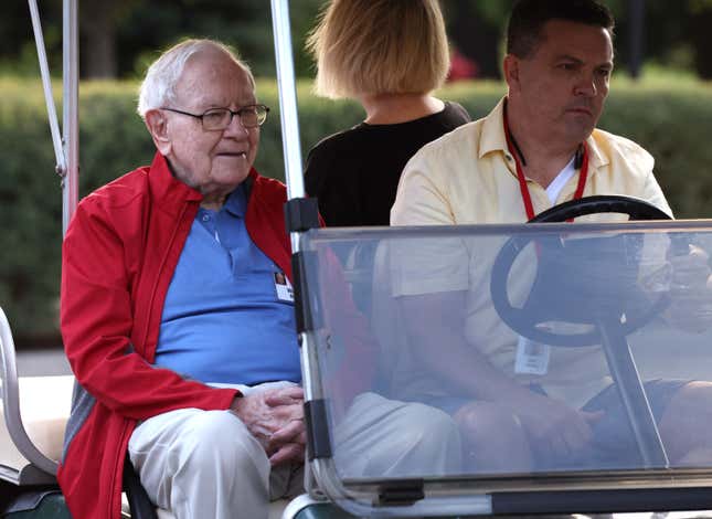 Warren Buffett sits inside a golf cart with his hands clasped in front of him.