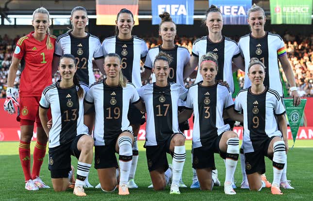 Two rows of women, one standing, one kneeling in front, wearing matching black and white uniforms, pose for the camera. 
