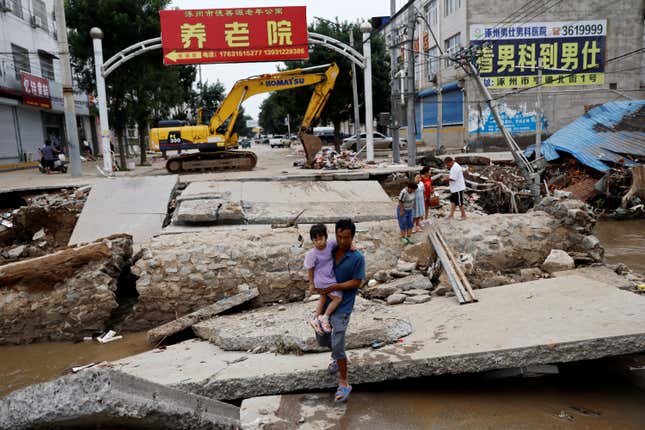 A man holding a child walks across a damaged bridge after the rains and floods brought by remnants of Typhoon Doksuri, in Zhuozhou, Hebei province, China August 7, 2023