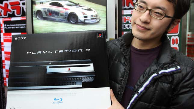 A man in a black jacket and glasses holds up a PlayStation 3. 