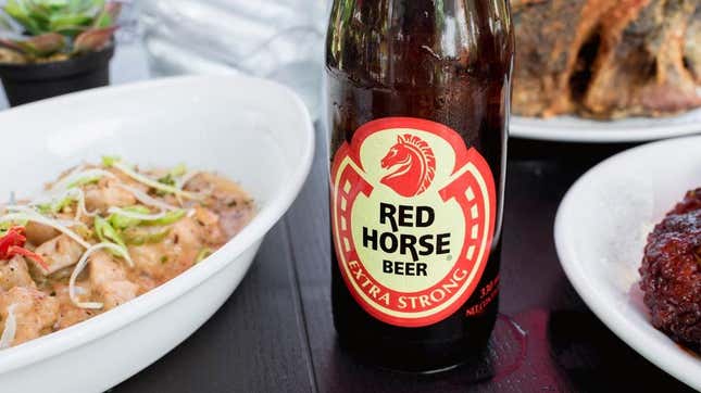 Red Horse Beer bottle beside Filipino food dishes