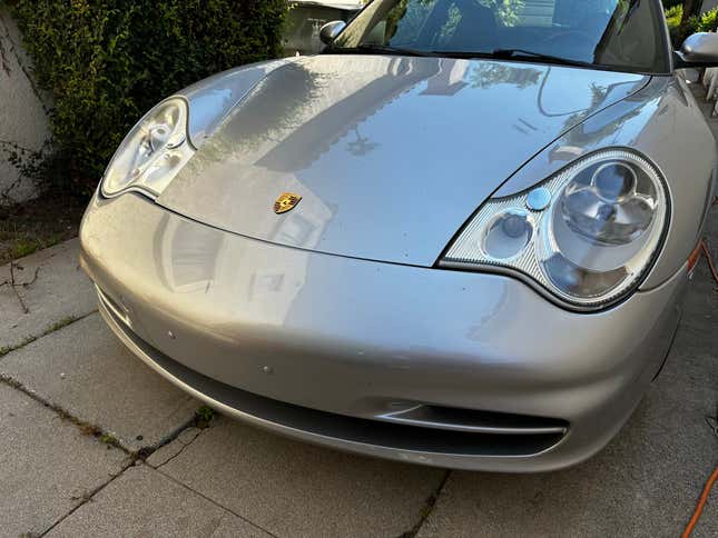 A dirty silver 2003 Porsche 911 sits in a driveway with new-looking headlights