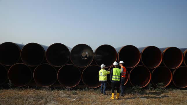 Workers stand in front of stacked pipes for a natural gas pipeline.