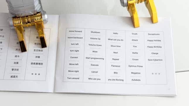 A shot of Robosen and Hasbro's Transformers Grimlock Auto-Converting Robot Flagship Collector’s Edition's feet standing on the instruction manual showing the various voice commands available.