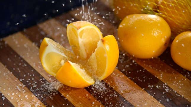Salt being sprinkled onto a sliced lemon on a cutting board in order to preserve it