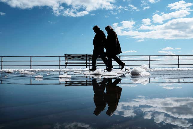 A couple walks by puddles from snow melt along the Coney Island boardwalk