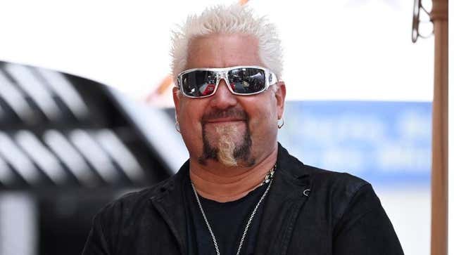 Guy Fieri in sunglasses and a black jacket, smiling