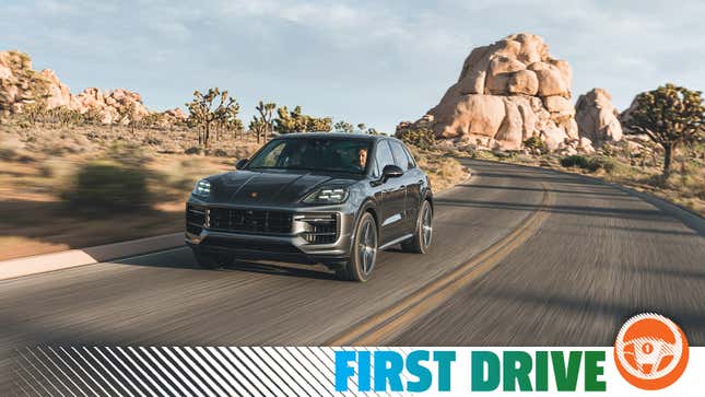 The 2024 Porsche Cayenne S in gray is driving in front of some big rocks in the desert.