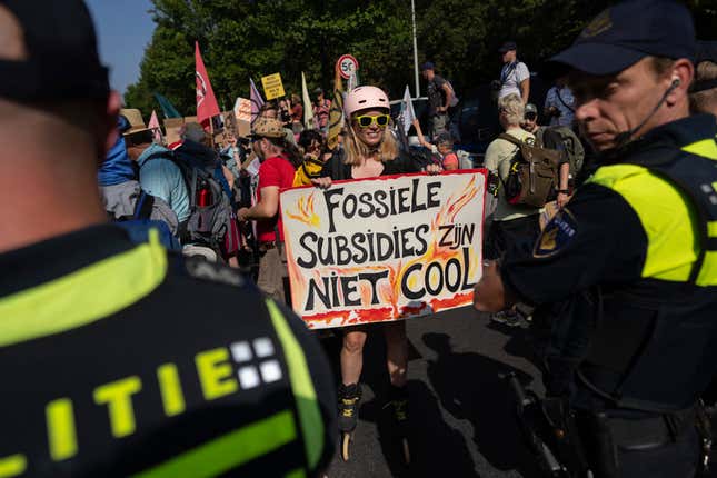 A protestor holds a sign reading 'Fossil Subsidies Are Not Cool' as they block a highway during a climate protest of Extinction Rebellion and other activists near the Dutch parliament in The Hague, Netherlands, Saturday, Sept. 9, 2023. (AP Photo/Peter Dejong)