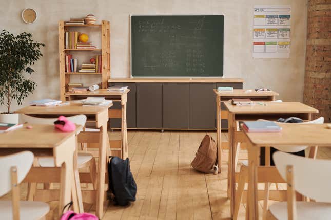 Wide angle background image of wooden school desks in a row facing blackboard in an empty classroom