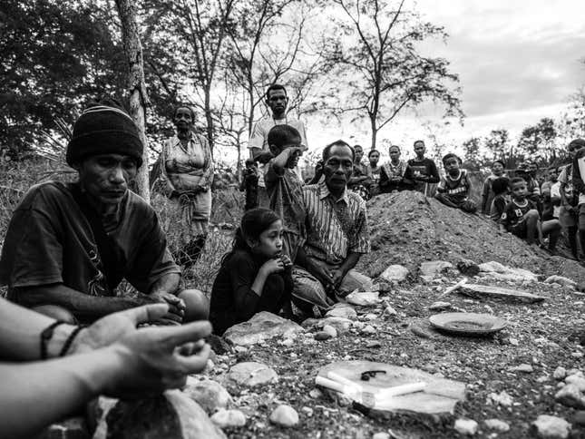Mikhael and his grandchildren, together with other villagers, pray at a makeshift grave for Dolfina.