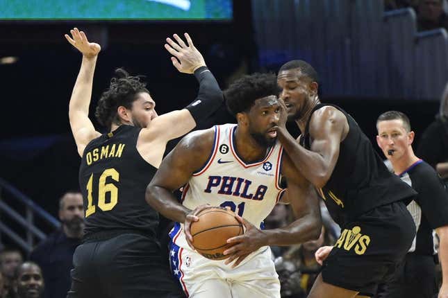 Mar 15, 2023; Cleveland, Ohio, USA; Philadelphia 76ers center Joel Embiid (21) looks to pass while defended by Cleveland Cavaliers forward Cedi Osman (16) and forward Evan Mobley (4) in the second quarter at Rocket Mortgage FieldHouse.